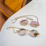 Two pairs of sunglasses on a white surface with a person in a yellow swimsuit partially visible.