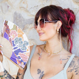 Woman with tattoos holding a colorful fan against a stone wall.