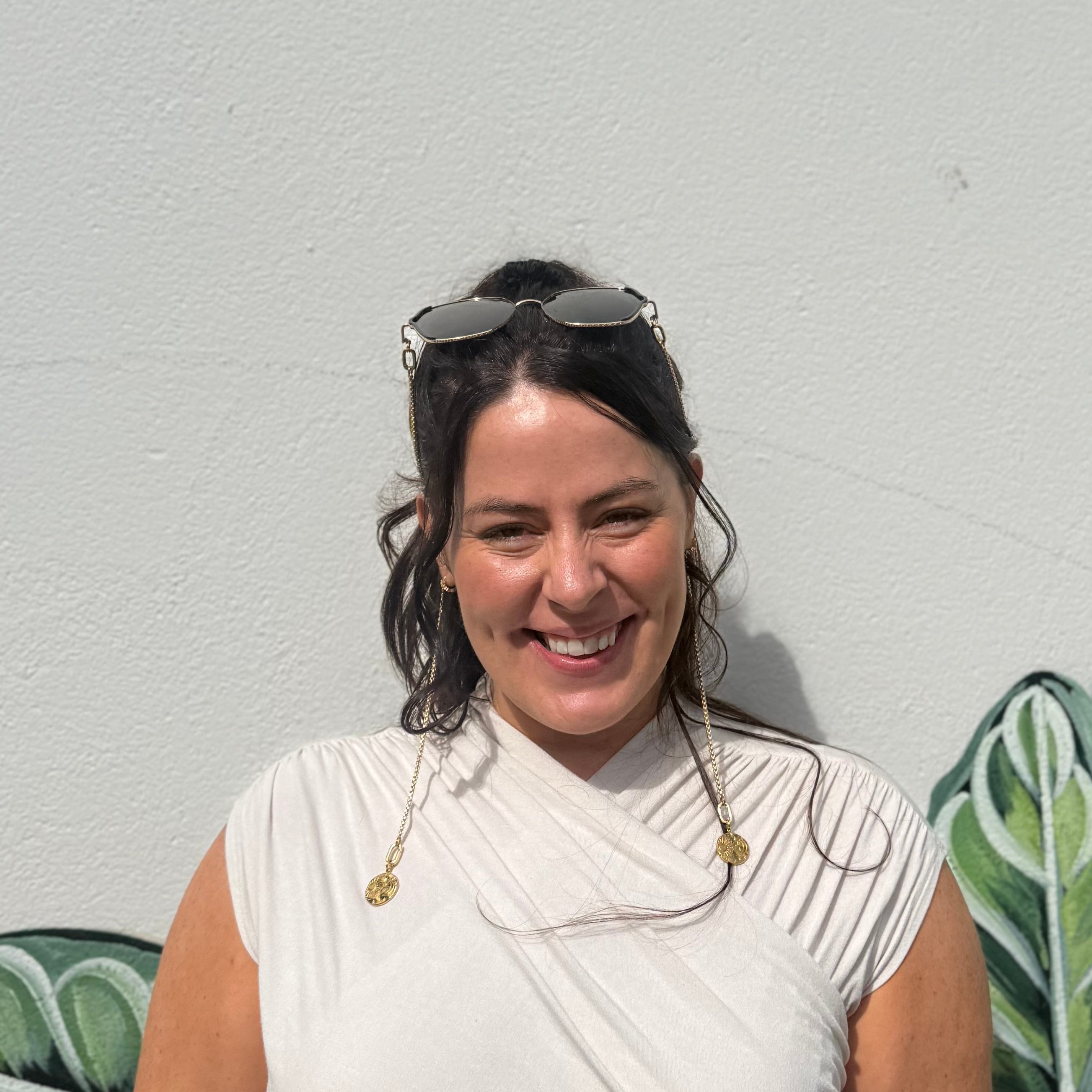 Woman standing in front of a wall with green leafy patterns wearing Ziggy modular sunglasses on her head